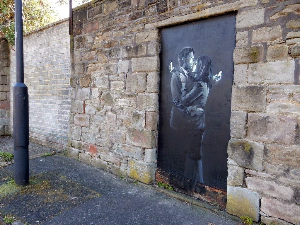 Banksy, Mobile Lovers, Bristol, 2014. Due persone sono fisicamente vicinissime, ma la loro attenzione è altrove.